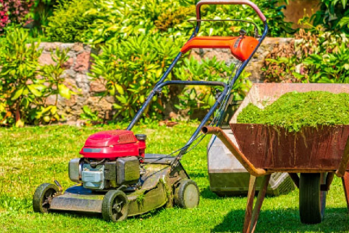 Ein Rasenmäher und eine Schubkarre mit Grasschnitt.